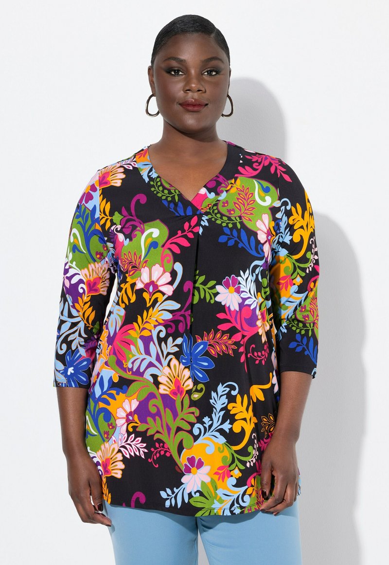 Färgglad blommig tunika med V-ringning och trekvartslånga ärmar, tillverkad av ett mjukt tyg med svart bakgrund och livfulla mönster.