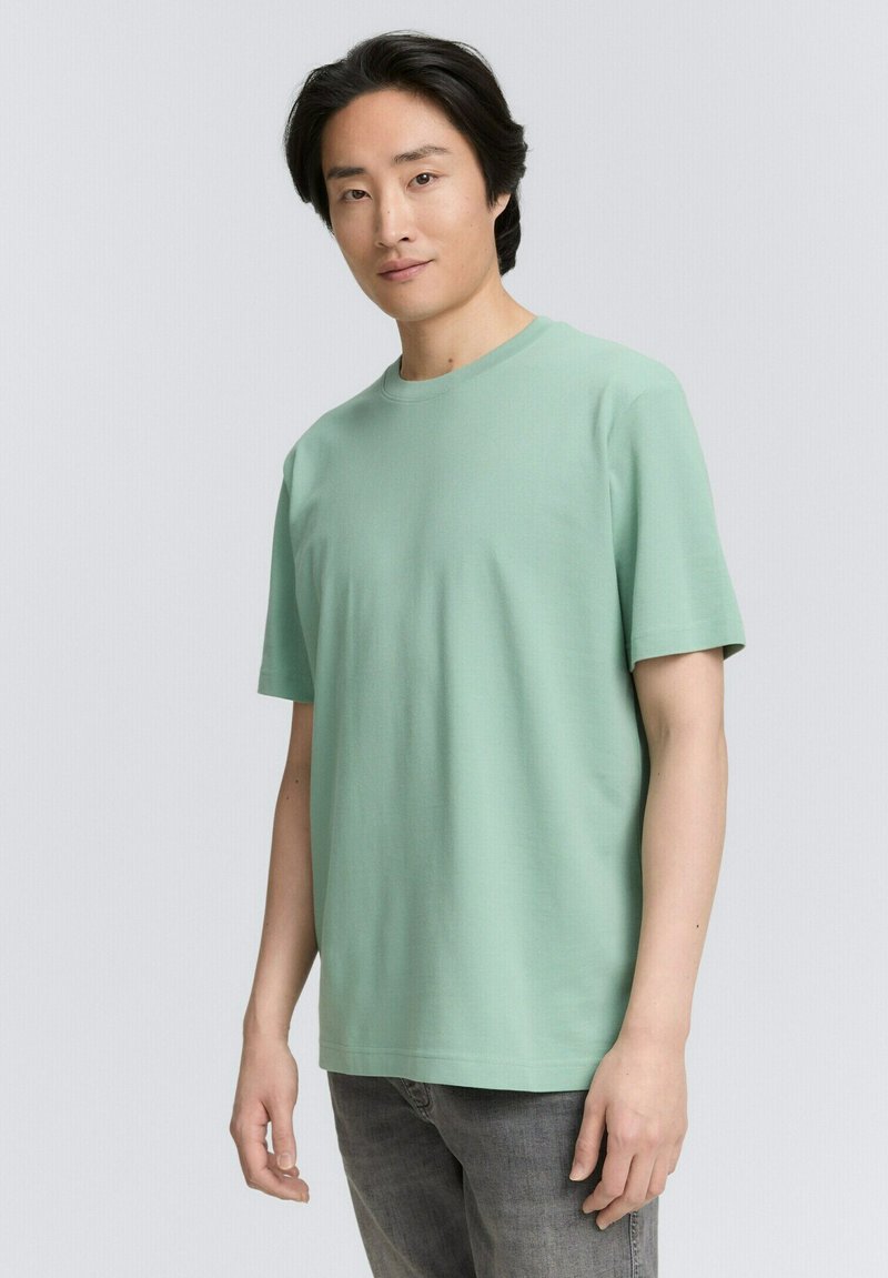 Camiseta de algodón verde clara con mangas cortas, cuello redondo y un corte holgado. Textura suave, sin patrones o acentos visibles.