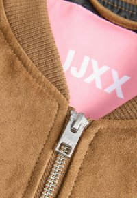 Brun ruskindsjakke med en ribbet krave, sølvlynlås og en lyserød indvendig foring med hvid tekst. Tekstureret overflade med glat hardware.