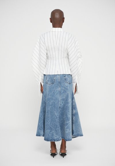 Person wearing white long-sleeve shirt with vertical stripes and calf-length blue denim skirt, standing facing away on white background.
