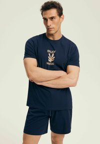 Granatowa bawełniana koszulka z beżowym nadrukiem "CIESZ SIĘ PRZYRODĄ" oraz pasującymi granatowymi szortami, o prostym kroju i luźnym fasonie.