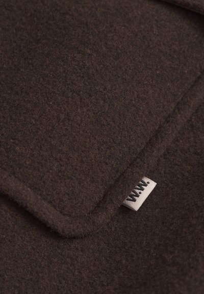 Textil de fieltro marrón con una textura suave, que presenta un borde doblado y una pequeña etiqueta de tela que muestra las letras "W.W." en negro.