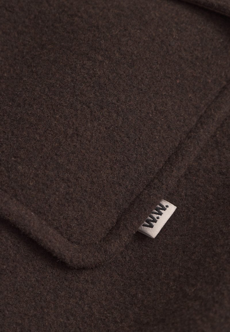 Bruin vilttextiel met een zachte textuur, voorzien van een gevouwen rand en een klein label met de letters "W.W." in het zwart.