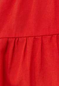 Tessuto di un rosso brillante con una superficie liscia, caratterizzato da piccole pieghe lungo la cucitura, che mette in mostra un design monocromatico vibrante.