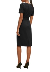 Schwarz enganliegendes Kleid mit kurzen Ärmeln, mittellang, Taille mit Bindegürtel und Reißverschluss im Rücken. Glatte Textur, minimalistische Details und eine klassische Silhouette.