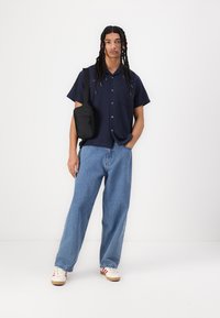 Navy short-sleeve button-up shirt, light blue loose-fit jeans, black shoulder bag, and white sneakers with red accents.