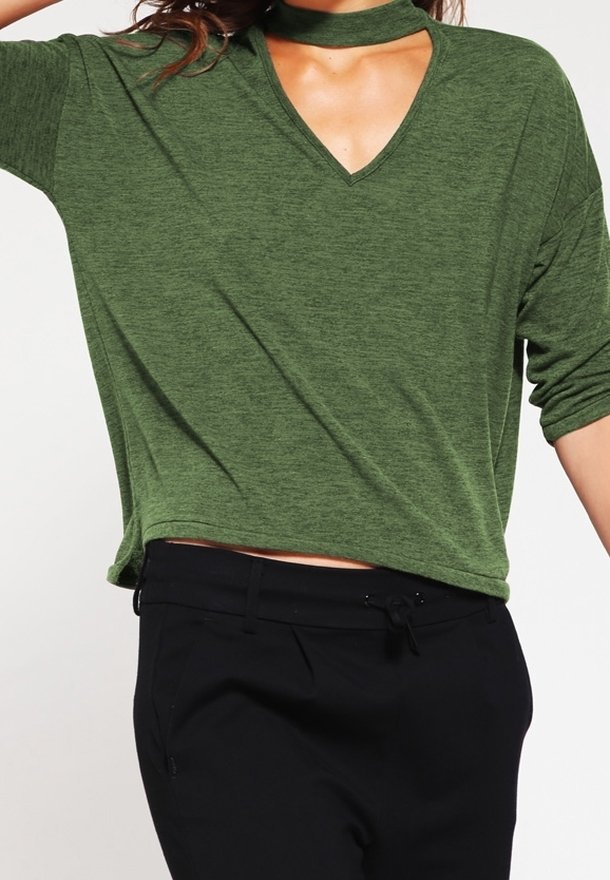 Grünes V-Ausschnitt-Top mit einem Choker-Detail, aus weichem Stoff, mit kurzen Ärmeln und lockerer Passform. Kombiniert mit schwarzen Hosen.