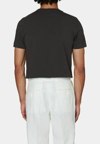 Maglietta nera a maniche corte con taglio dritto e una texture di cotone morbido, abbinata a pantaloni chiari plissettati.