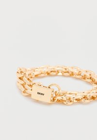 Kuldne kett käevõru, millel on pikendatud lingid ja ristkülikukujuline pandlaga, millel on peen teemantdekoor ja graveeritud DKNY logo.