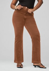 Pantalones de pana marrones de campana con cintura alta, que cuentan con bolsillos delanteros y cierre de botón. La tela tiene un acabado suave y texturizado.