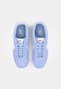 Gaiši zili sporta apavi, izgatavoti no teksturēta materiāla, ar baltiem šņorēm, baltu swoosh logo un mīkstu iekšējo oderi.