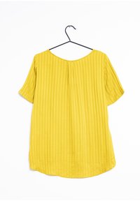 Top giallo a maniche corte realizzato in tessuto testurizzato con strisce verticali e scollatura tonda, appeso a un gancio nero su uno sfondo bianco.