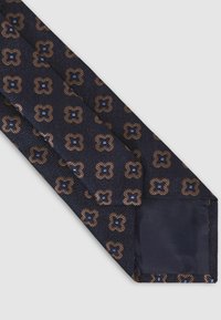 Cravat bleumarin cu un model texturat de forme florale maronii suprapuse, fiecare având un accent rectangular albastru. Părțile interioare netede sunt de culoare bleumarin solid.