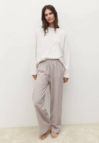Maglietta beige chiaro a maniche lunghe abbinata a pantaloni da pigiama larghi a righe rosa e bianche, dotati di una cintura elastica e di una texture morbida.