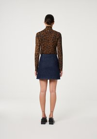 Langärmliges braunes Oberteil mit schwarzem Herzmuster, kombiniert mit einem dunkelblauen Jeansrock. Dunkle Schuhe runden das Outfit ab.