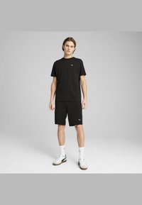 Black athletic outfit featuring a crew-neck t-shirt and shorts, both with a small white Puma logo. Worn with white socks and shoes.