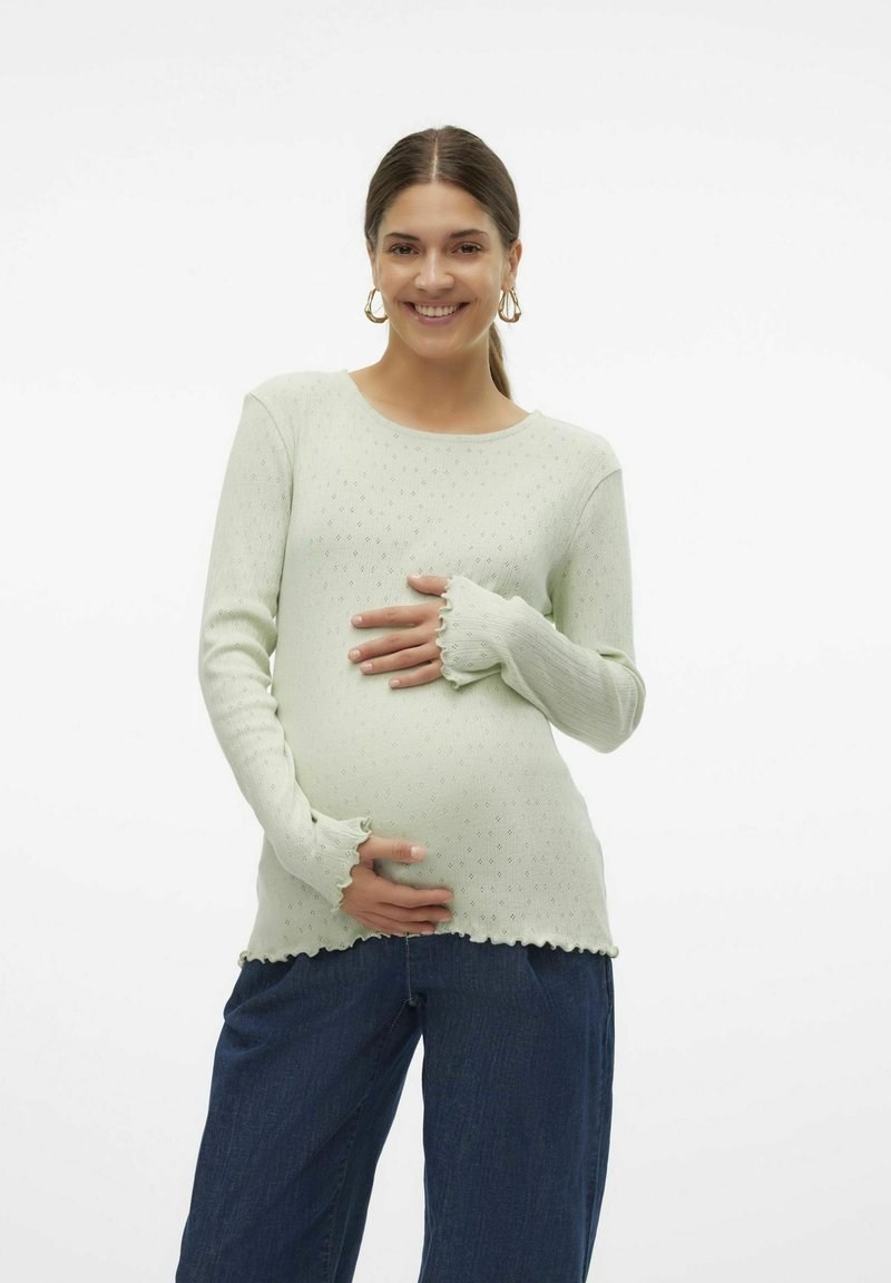 Pullover verde chiaro a maniche lunghe con un motivo texturizzato e orli arruffati sulle maniche, abbinato a jeans blu scuro dal fit morbido.