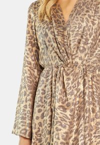 Kleid mit Leopardenmuster und Wickeldesign in Gold- und Brauntönen, ausgestattet mit einem strukturierten Stoff und langen Ärmeln. Detaillierter Taillengürtel.