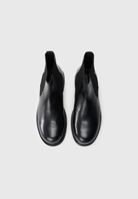 Botines de cuero negro con paneles laterales elásticos, punta redonda y suela plana. Textura suave con un diseño minimalista.