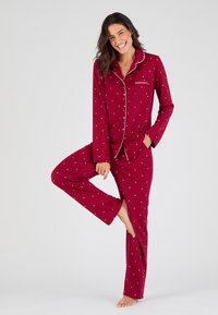 Ensemble de pyjama bourgogne en tissu doux avec des pois blancs, comprenant un haut à boutons avec poche et un pantalon long. Texture lisse et coupe décontractée.