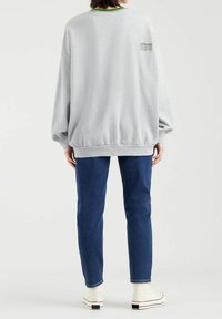 Persona vestida con un sudadera gris oversized con el texto "Establecido en 1873", jeans azules y zapatillas altas blancas, de pie de espaldas.