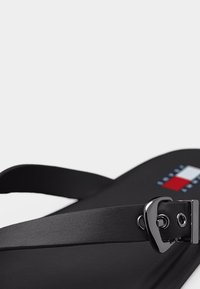 Μαύρο σανδάλι-σαγιονάρα με ρυθμιζόμενο λουράκι και ασημένια αγκράφα, με μικρό λογότυπο σε κόκκινο, λευκό και μπλε στην σόλα.