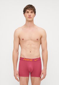 Piros boxeralsó sárga Nike logóval a derékpánton. Rugalmas anyagból készült, szoros szabású, sima textúrával.