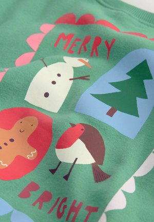 Grüner Stoff mit einem verspielten Design, das einen Schneemann, einen Lebkuchenmann, einen roten Vogel und einen Weihnachtsbaum zeigt. Der Text lautet "FRÖHLICHE WEIHNACHTEN."