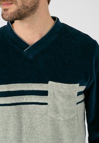 Camiseta azul marino de cuello en V con rayas horizontales grises y un bolsillo en el pecho, con tejido suave y un corte relajado.