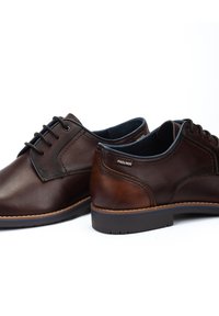 Zapatos de cuero marrón con punta redondeada, diseño con cordones, costuras en contraste y acentos texturizados. Presentan un acabado suave y suela duradera.