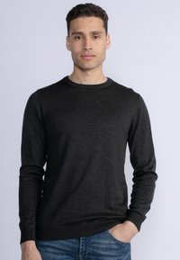 Dark gray, long-sleeve crewneck sweater with ribbed cuffs and hem, made from soft material. Worn over fitted blue jeans.
