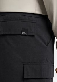 Zwarte cargobroek van textuurstof met zij- en achterzakken. Heeft een kleine Jack Wolfskin logo-tag op de zak gestikt.
