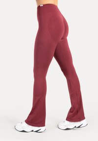 Leggings taille haute couleur bordeaux avec une texture lisse, bas évasé et détails subtils de contour à l'arrière, accompagnés de baskets blanches.