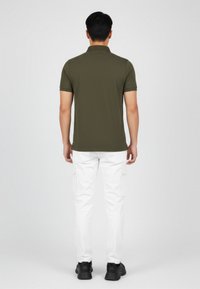 Olivgrünes Polohemd mit kurzen Ärmeln, kombiniert mit weißen Cargo-Hosen und schwarzen Sneakers. Sichtbare Nähte und Taschen an den Hosen.