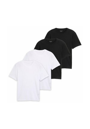 Mann mit kurzen lockigen Haaren, der ein schlichtes schwarzes T-Shirt mit kurzen Ärmeln und beige Hosen trägt, steht vor einem einfarbigen hellen Hintergrund.
