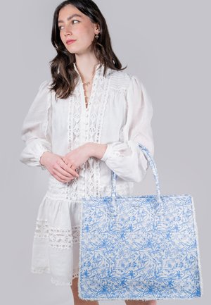 Large tote bag in blue floral print on white fabric with textured edges, featuring sturdy handles and a spacious design for carrying items.
