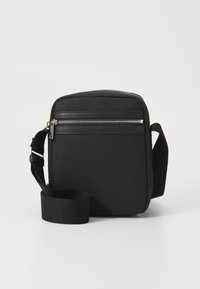Sac bandoulière noir en toile avec fermeture éclair, panneau avant texturé et sangle en tissu réglable.