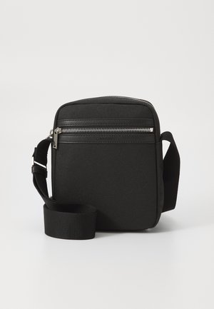Sac bandoulière noir en toile avec fermeture éclair, panneau avant texturé et sangle en tissu réglable.