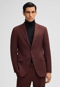 Completo bordeaux con rever a punta, due tasche frontali e due bottoni. Indossato sopra un dolcevita nero. Tessuto liscio con una sottile texture.