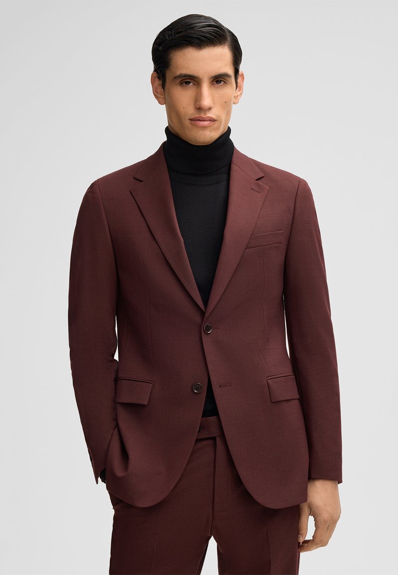 Completo bordeaux con rever a punta, due tasche frontali e due bottoni. Indossato sopra un dolcevita nero. Tessuto liscio con una sottile texture.