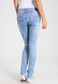 Jeans ajustados de color azul claro con una textura suave, que presentan sutiles costuras en los bolsillos traseros y un parche de marca de cuero sintético en la cintura.