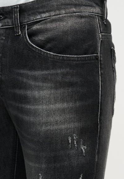 Κοντινό πλάνο μαύρου ξεθωριασμένου τζιν με μπροστινή τσέπη και διακριτικές φθορές στο μηρό.