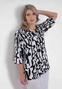 Chemise à motif noir et blanc avec un tissu doux, des manches trois-quarts et un col à boutonner, présentant un design abstrait.