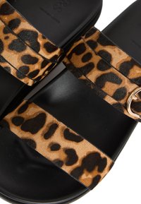 Leopardmönstrade sandaler med svart sula. Två mjuka remmar i brun och svart mönstring. Har en guldfärgad spänne för justering.