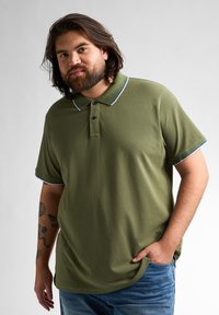 Oliwkowa koszulka polo wykonana z bawełny o miękkiej fakturze, z klasycznym kołnierzykiem, dwoma guzikami oraz niebieskimi wykończeniami na rękawach i kołnierzyku.