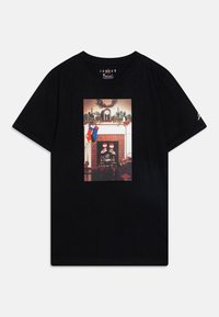 Black cotton t-shirt featuring a central graphic of a holiday-themed fireplace with stockings and shoes. Short sleeves and crew neck design.