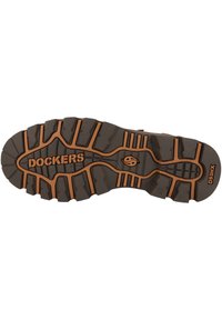 Suela de zapato de goma marrón oscuro con un patrón de relieve intrincado, con acentos naranjas y el nombre de la marca "DOCKERS", modelo "D53HX."