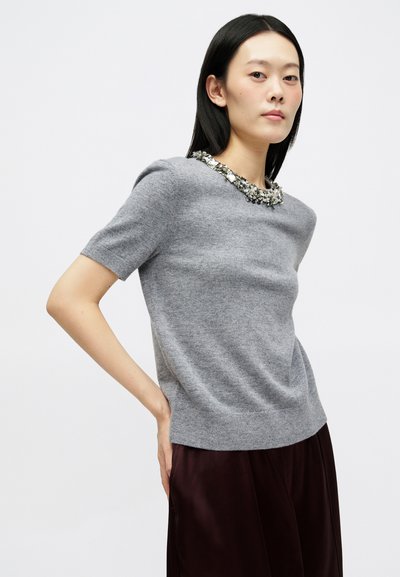 Γκρί πουλόβερ με κοντό μανίκι κατασκευασμένο από μαλακό ύφασμα, χαρακτηρισμένο από μια διακοσμητική κολάρο με κοσμήματα και εφαρμοστή γραμμή. Λείο υφή.