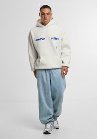 Felpa di cotone grigio chiaro con testo blu "another" e "cotton", abbinata a jeans larghi di jeans blu chiaro e sneakers grigie.