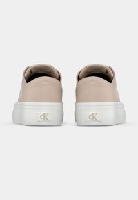 Μπεζ πάνινα παπούτσια με λευκή λαστιχένια σόλα, με λεπτομέρεια λογότυπου στο πίσω μέρος και ομαλή υφή. Απλός, χαμηλού προφίλ σχεδιασμός.